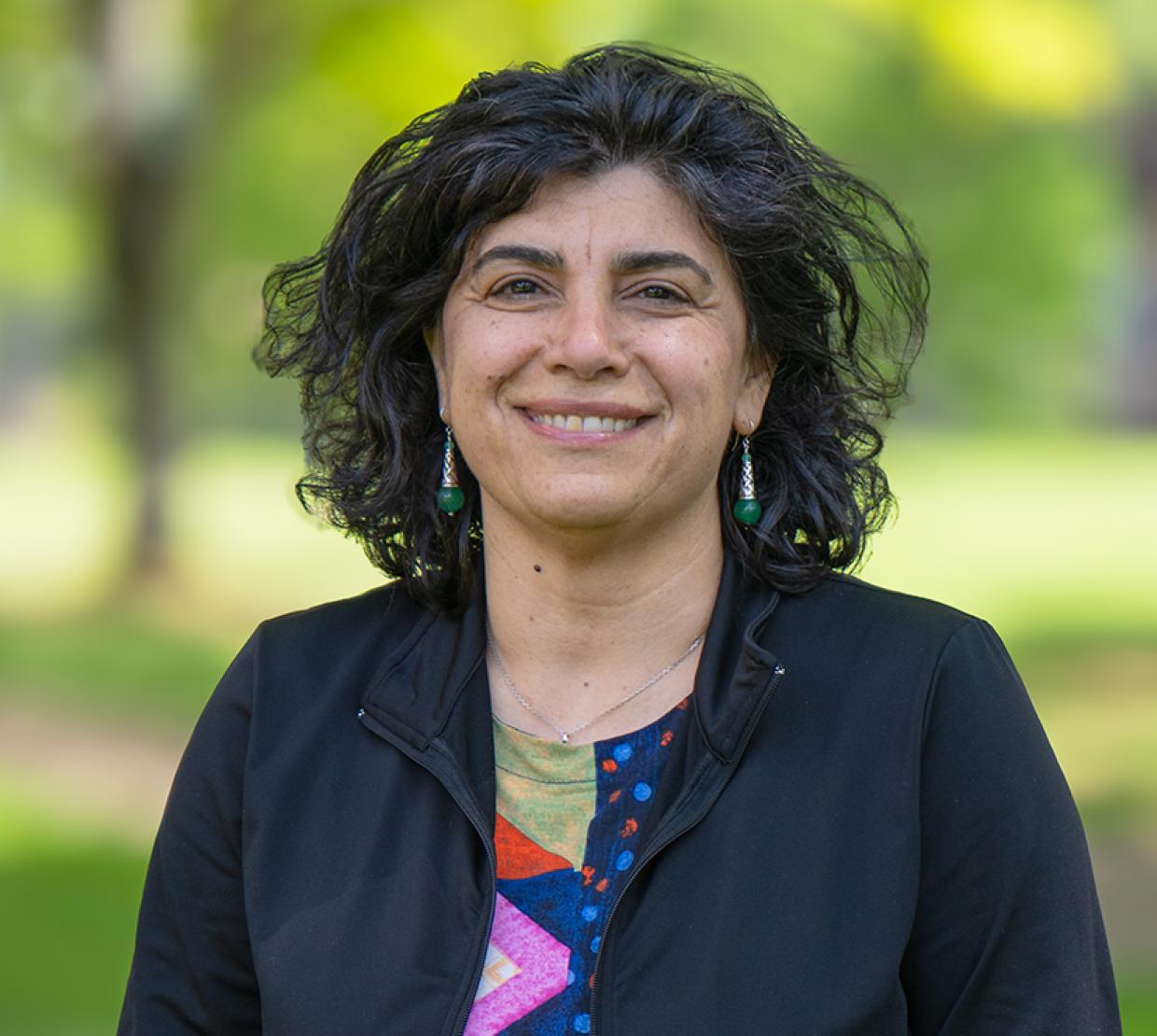 A woman in a colored print shirt and black jacket smiles for a headshot.