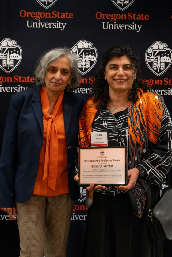 Two women smiling and one holding an award.