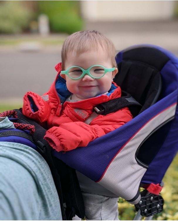 Baby with glasses in stroller smiling at camera.