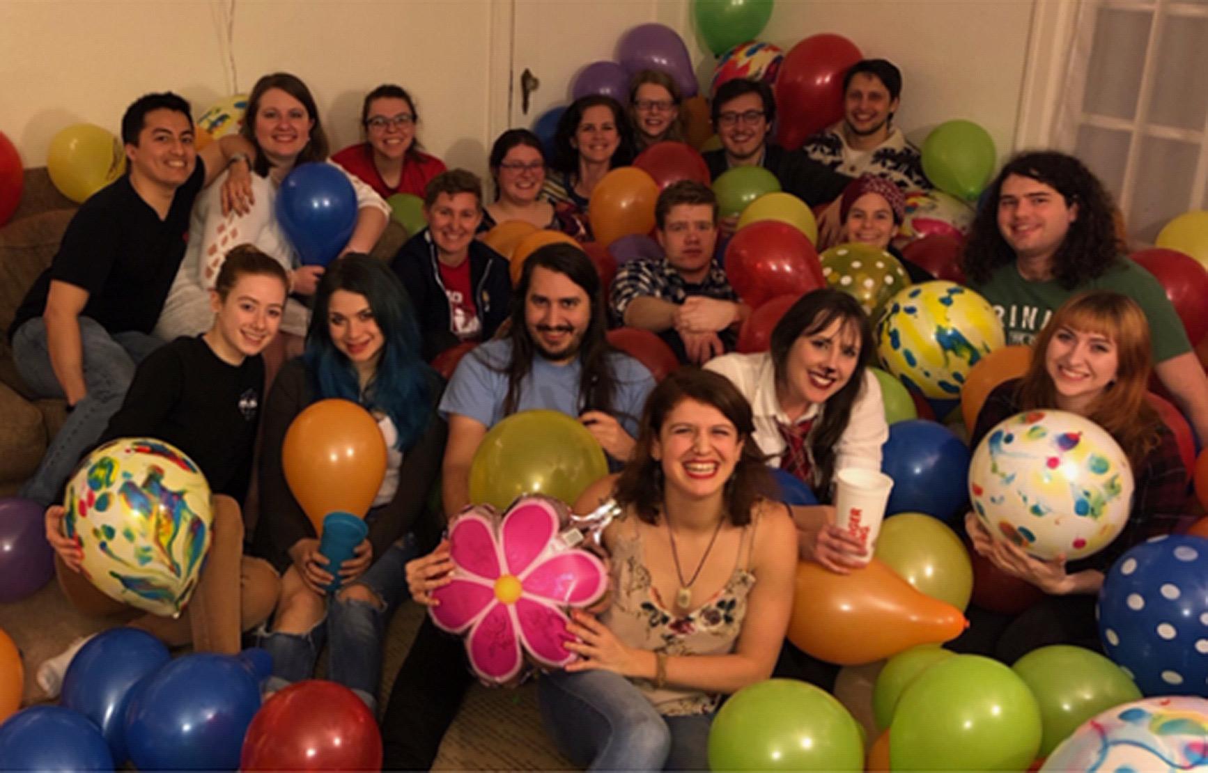 A group photo of the Graduate Student Association members in a living room sitting in a pile of balloons.