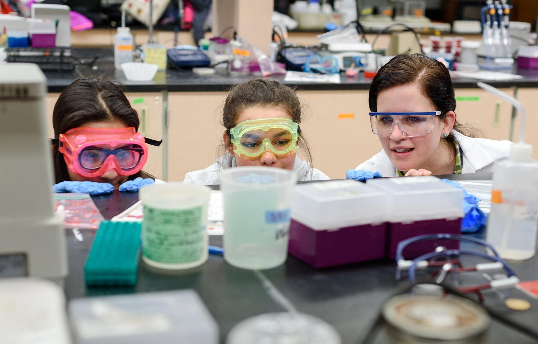 A BB Student and two female middle school students, all crouched in front of a lab experiment.