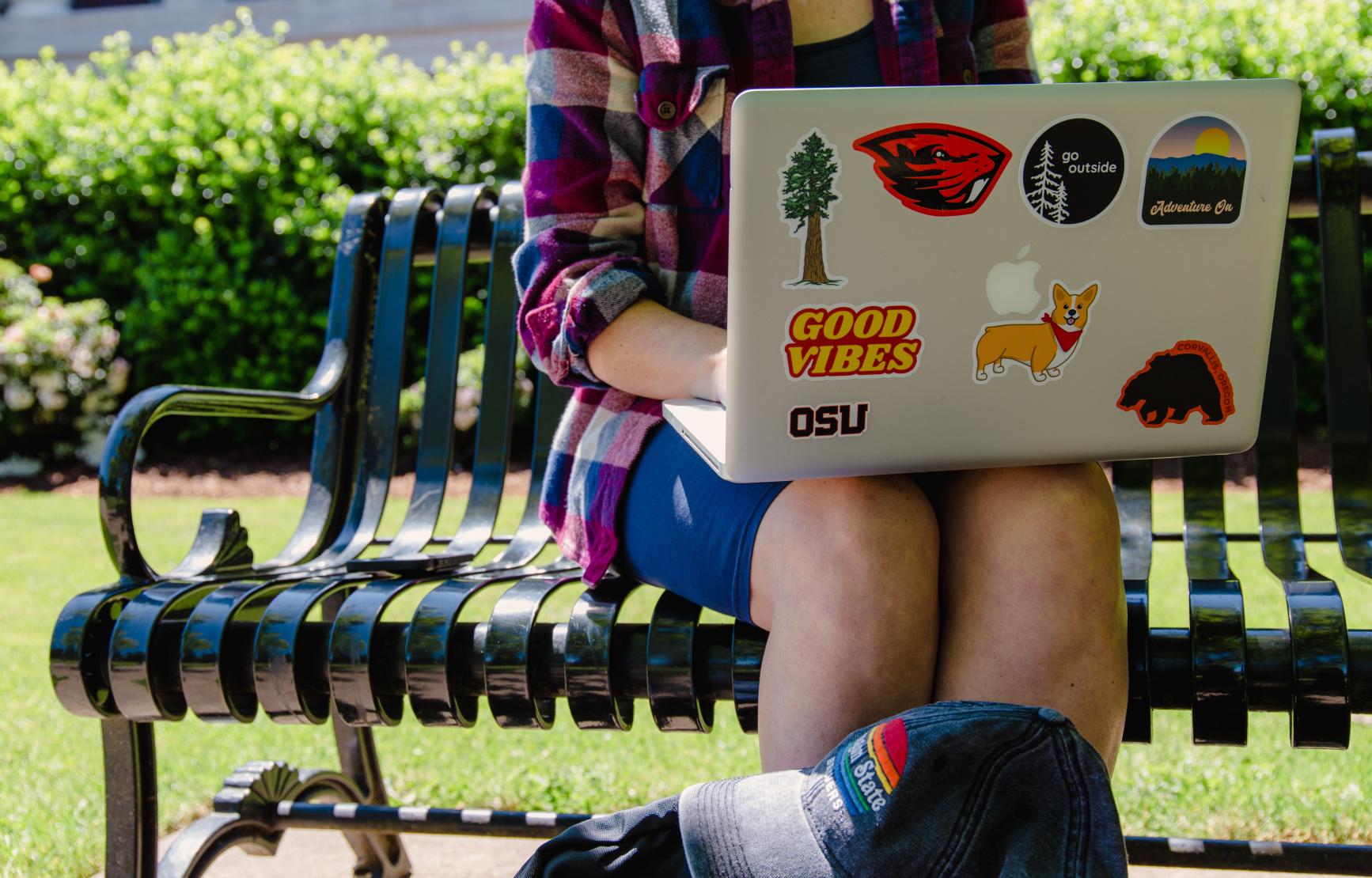 A student using their laptop while sitting on a bench outdoors.