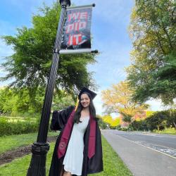 Alyssa Pratt stands in front of a pole with a sign that reads "We did it." She is wearing her graduation cap and gown.
