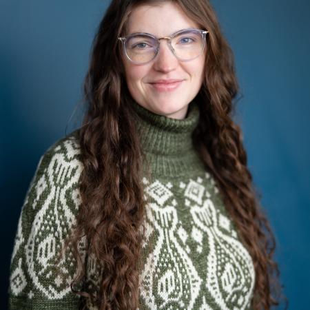 Headshot of a woman in a green fish sweater with long brown hair.
