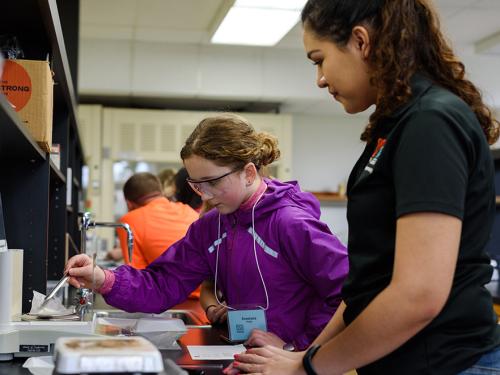 A female middle school student working with a college student in a lab.