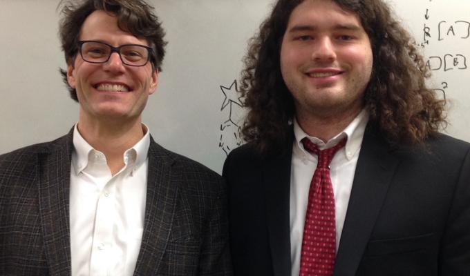 Ryan Mehl and Robert J Blizzard standing in front of white board in suits