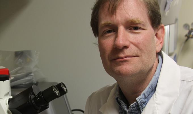 Adrian Gombart in lab coat next to microscope