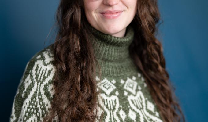 Headshot of a woman in a green fish sweater with long brown hair.