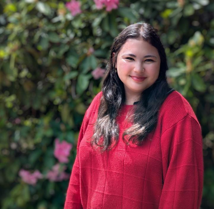 Emily Kaneshiro smiles in front of flowery bushes.