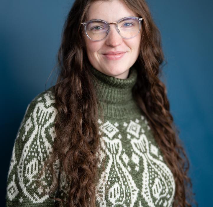 Headshot of a woman in a green fish sweater with long brown hair.