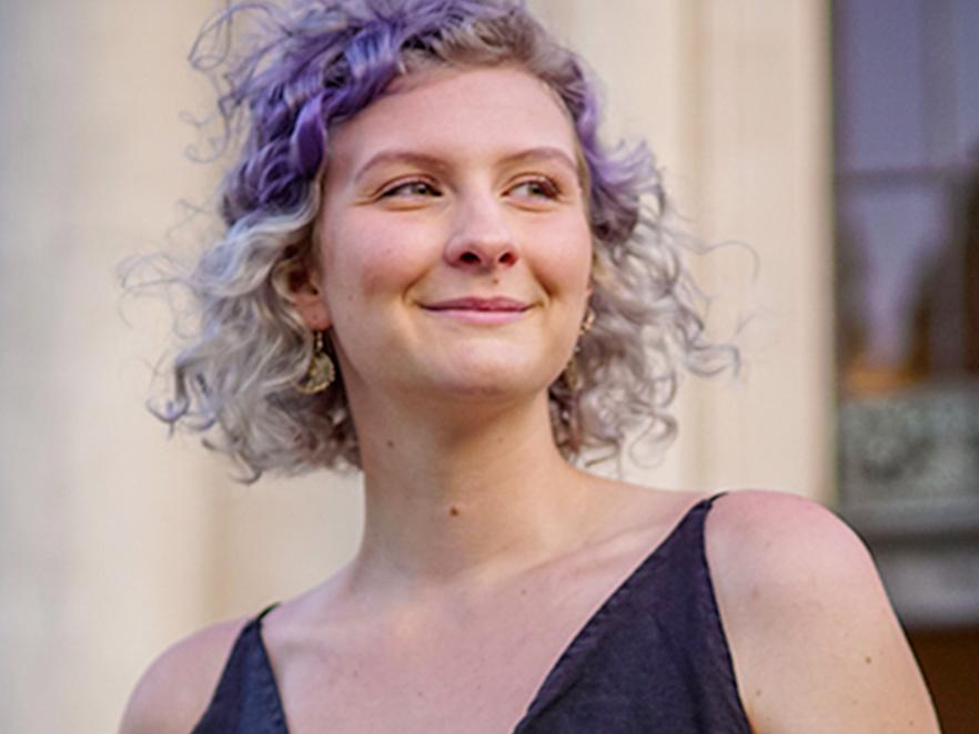 A smiling woman with colorful, curly hair standing in front of the Memorial Union